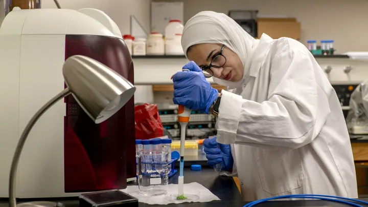 Woman in lab coat using pipette to transfer a liquid.