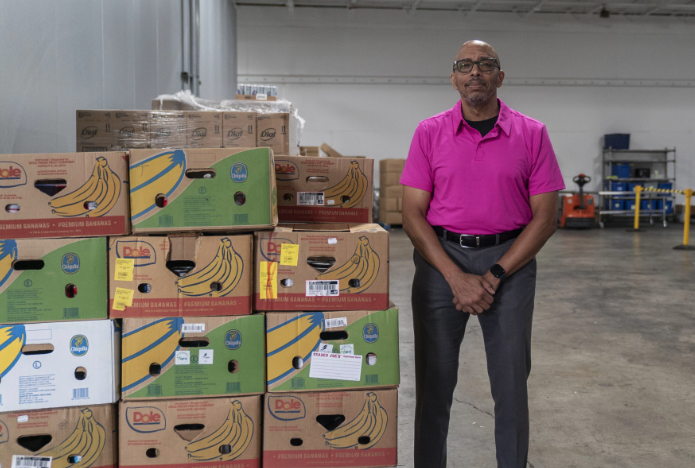 Man standing next to boxes of bananas in warehouse.